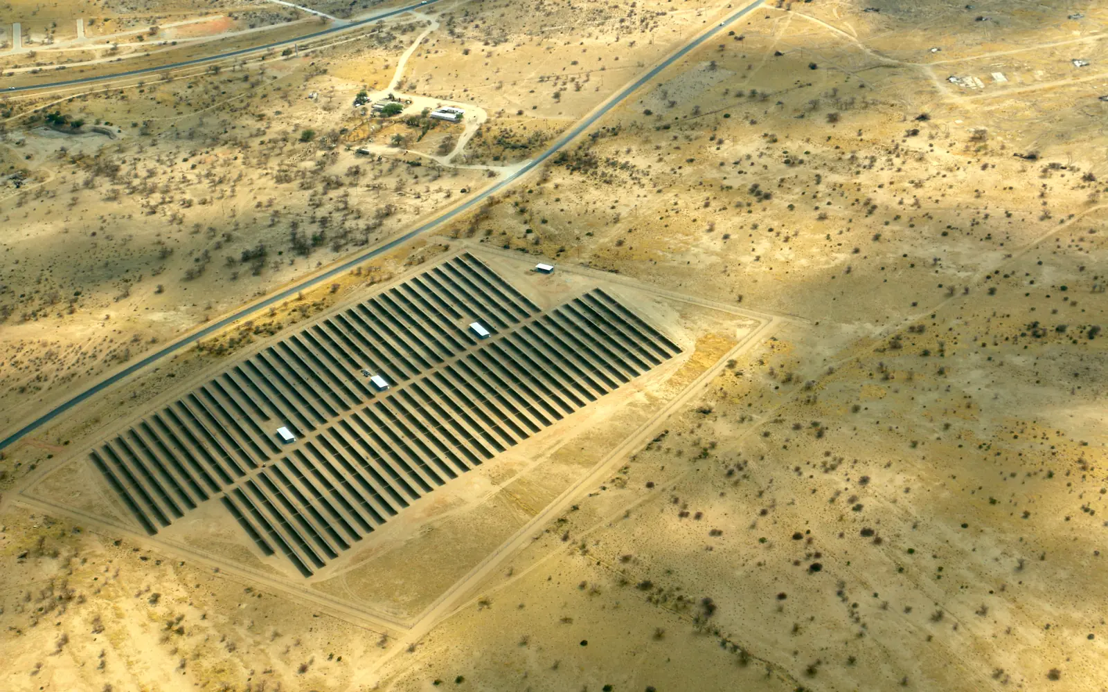 A solar plant seen from the air, rows of panels set in dry bushveld