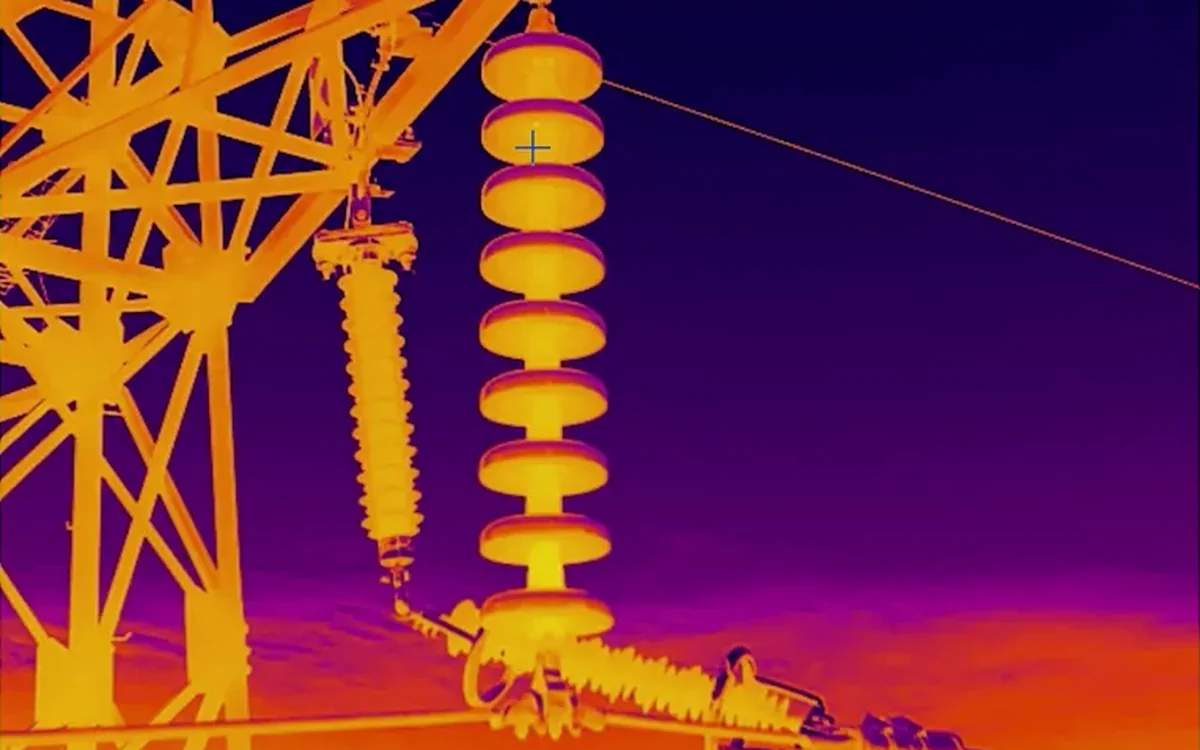 A thermal frame from the same turret: a substation insulator string glowing hot against a cold sky, the fittings clearly warmer than the steel around them