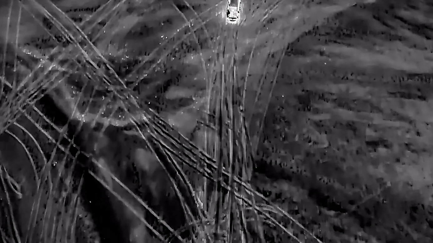 An aerial thermal view: cold ground in grey, a vehicle glowing white hot against it